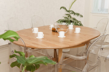 Cozy dining setting featuring a round wooden table surrounded by transparent chairs, complemented by lush green potted plants, creating a warm and inviting interior atmosphere.