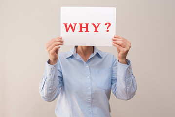 Woman holding white sign with red question word why, expressing doubt and uncertainty on beige...