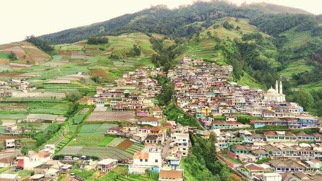 Drone view of village on lush mountain slope called Dusun Butuh surrounded by agricultural fields