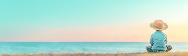 Fototapeta premium Boy in straw hat and with camera sitting on the sea beach. Summer vacation concept.