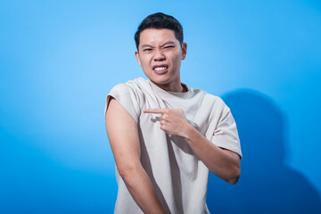 Asian man in a white t-shirt holding his shoulder with a painful expression, eyes squinting and...