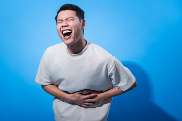 Asian man in a plain white t-shirt clutches his stomach with both hands and screams in pain, eyes...