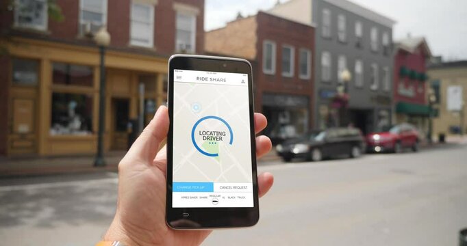 A man holds a smartphone running a ride sharing app. The screen reads Locating Driver. Fictional interface. Pittsburgh suburbs.  	