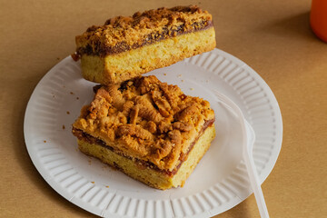 A golden-brown pie with jam and crumbly topping on a plate surrounded by disposable utensils. A symbol of quick preparation and high-calorie baking. Fast homemade preparation of delicious meals.