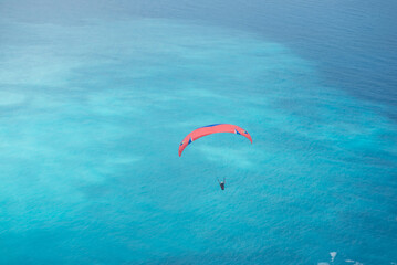Paraglider soaring over turquoise sea with scenic coastal landscape