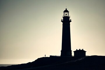 Silhouette of Lighthouse Against Sunset Sky Near Coastal Landscape