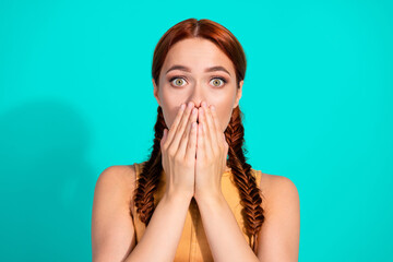 Young woman in a charming pose expressing surprise with hands covering her mouth against a vibrant...