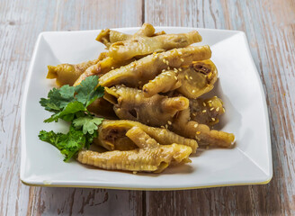 Braised chicken feet with savory sauce, sesame seeds and cilantro served in plate on Wood Table Close up Side view of Hong Kong food