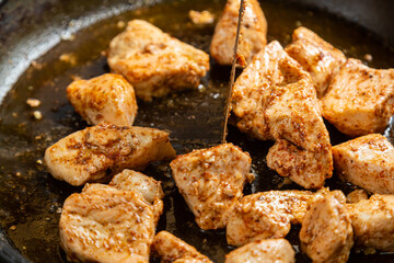 Chicken fillet pieces are fried in a frying pan in sauce and spices