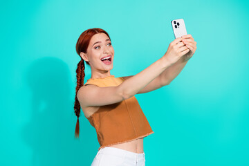 Cheerful Young Woman Capturing a Selfie with Smart Phone Against Vibrant Teal Background in Casual...
