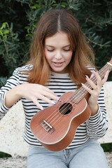 Young Woman Tunes The Ukulele Musical Instrument In A Park Outside