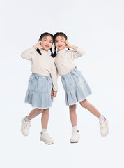 Twin girls in matching outfits posing with heart hands, standing side-by-side on a clean, white background.