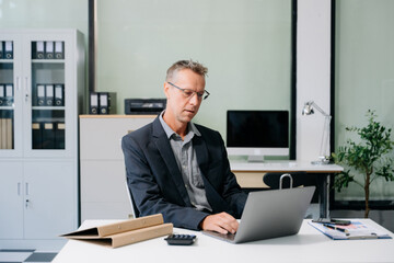 Obraz premium Confident businessman working on finance analysis with a tablet and laptop at office desk.