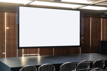 Blank projection screen in a modern conference room with stage setup and transparent chairs. Ideal...