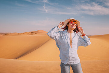 Cheerful tourist holding her hat and basking in the warm sun, reveling in the vast desert landscape...
