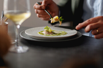 close view to man's hands holding a knife and fork, enjoying the haute cuisine dish in a restaurant 