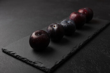 Juicy ripe fresh plum with water drops on black slate board. Seasonal fruit on black background. Selective focus, close-up.