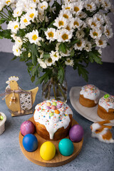 Easter kulich with candied fruits in white glaze with colorful sprinkles and painted eggs. Traditional Easter pastry. Easter holiday. Close-up, selective focus.
