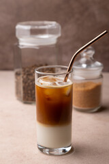 Coffee with coconut milk and ice cubes in a tall glass. Traditional non-alcoholic cold drink. In the background, a jar of coffee and a jar of sugar. Selective focus, close-up.