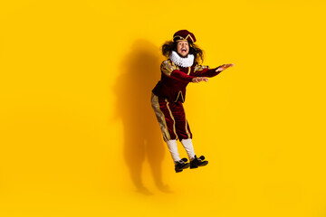 Young male actor in artistic medieval costume jumping against a vivid yellow backdrop symbolizing...