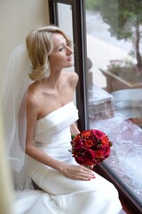 Happy bride in beautiful dress with red bouquet