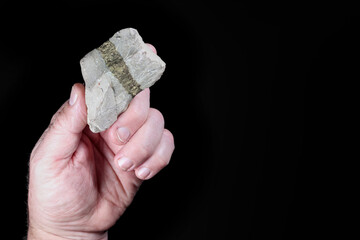 Gold mining ore. Rock with vein of iron pyrite (FeS2) held in hand. Black background. Fool's gold....