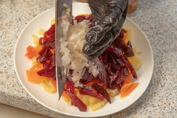 Chef adding chopped onions to boiled beets, potatoes and carrots to prepare vinaigrette salad....