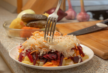 Chef adding sauerkraut to chopped onions and boiled beets, potatoes and carrots to prepare...