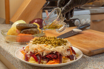 Chef cook adds vegetable oil to a vinaigrette salad made from sauerkraut, green peas. onions, boiled beets, potatoes and carrots. Close-up. Cooking