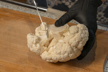 Chef cuts a head of cauliflower into florets on a kitchen cutting board. Close-up