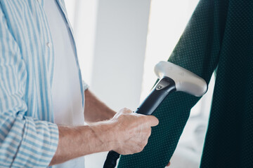 Elderly Man Using a Garment Steamer to Smooth Wrinkles in Clothing in a Cozy Indoor Setting