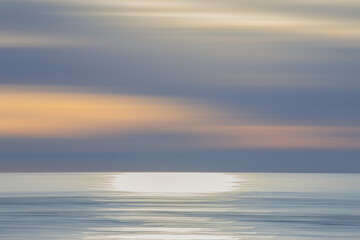 Abstract background of ocean at sunset, colourful sunrise with long exposure effect, horizontal motion blurred sea water with clouds, sea horizon at sunset with panning technique, pastel colours