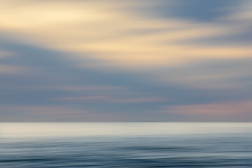 Abstract background of ocean at sunset, colourful sunrise with long exposure effect, horizontal motion blurred sea water with clouds, sea horizon at sunset with panning technique, pastel colours