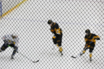Hockey players on the ice rink in a blur. In the foreground, a protective net