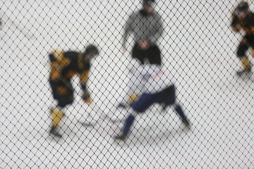 Hockey players on the ice rink in a blur. In the foreground, a protective net