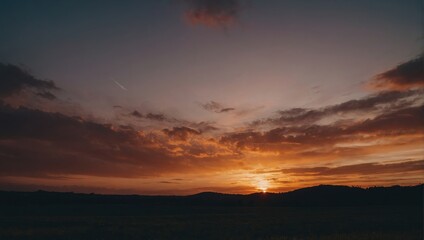Fototapeta premium Vivid sunset sky with orange clouds over a dark, expansive landscape creates a peaceful and evocative scene