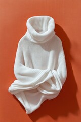 Obraz premium White turtleneck sweater folded on warm terracotta background minimalistic still life fashion autumn winter cozy clothing