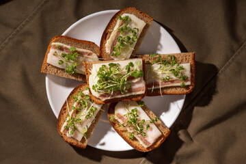A plate with several pieces of rye bread topped with salo and microgreens, presented on a rustic fabric backdrop.