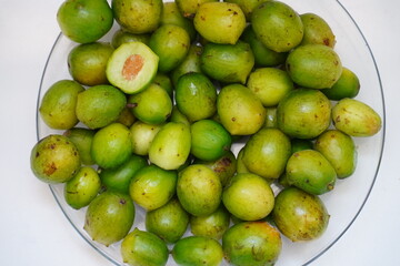 Green and ripe umbu fruits (Spondias tuberosa) on a plate. They are also known as Brazil plums. A fruit cut open in cross-section.  The fruits are edible, sweet and sour and also good for diabetes.