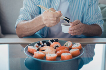 Elderly man enjoying sushi with chopsticks at home in a casual setting during daytime