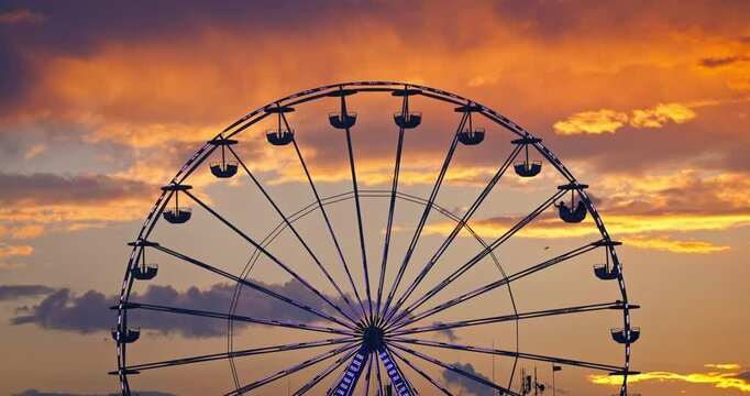 Carnaval ferris wheel in amusement park and scenic sunset clouds in sky silhouette