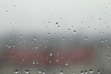 A close-up image of raindrops on a window, with the water droplets visibly clinging to the glass. The background could feature a blurred outdoor scene
