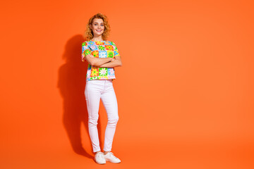 Smiling young woman in colorful floral print t-shirt posing confidently on vibrant orange backdrop, showcasing cheerful style