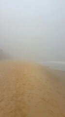 Foggy beach scene with empty sand, gentle waves, and a serene atmosphere in the background