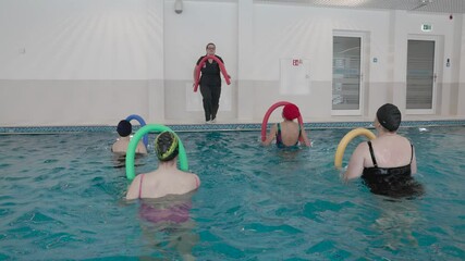 A group of individuals participates in an aquatic therapy session in a modern rehabilitation pool. The instructor, demonstrating exercises with a foam noodle, leads the session to improve strength, mo