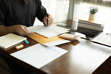 the businessman is sitting at a desk with a calculator and a stack of papers. She is looking at the...