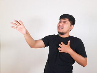 Handsome Asian man wearing a black shirt with a gesture of pain in his chest due to a heart attack and lung problems. Gesture asking for help