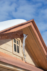 transparent icicle of ice on a spring day on the background of the roof of the house