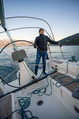 Young man captain standing at the helm and controls a sailboat during a journey by sea in winter time in Montenegro