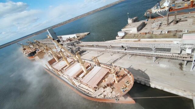 Wheat loading process captured from an fpv drone at a bulk carrier ship terminal on a sunny day